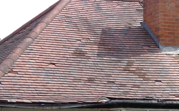 An older clay-tiled roof with several slipped and broken tiles near the eaves.