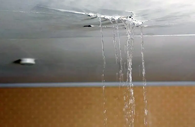 Water running through a split in a plaster ceiling and down the wall below it.