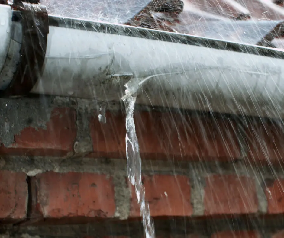 Water escaping from a leaking gutter joint and staining the brickwork underneath.