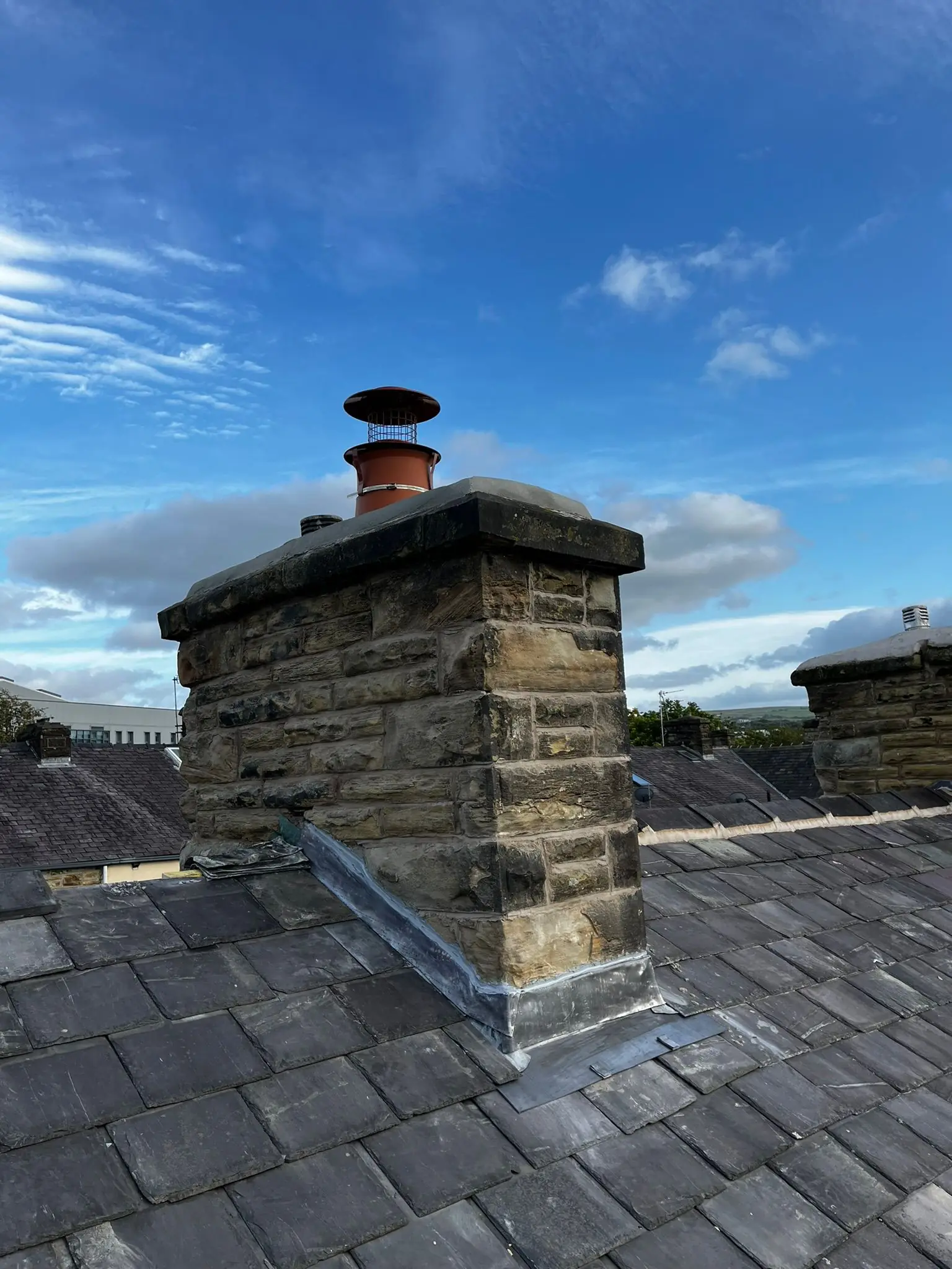 A stone chimney stack with lead flashing worked in around its base on a slate roof.